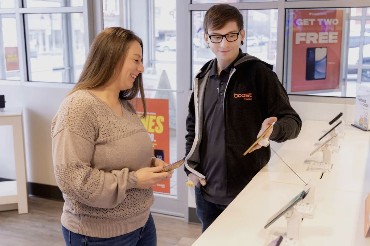 A Boost Mobile specialist helping a customer compare phones at the store counter