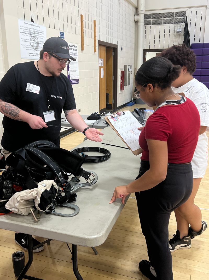 A One-Stop technician showing fiber optic cable to students holding Career Day worksheets