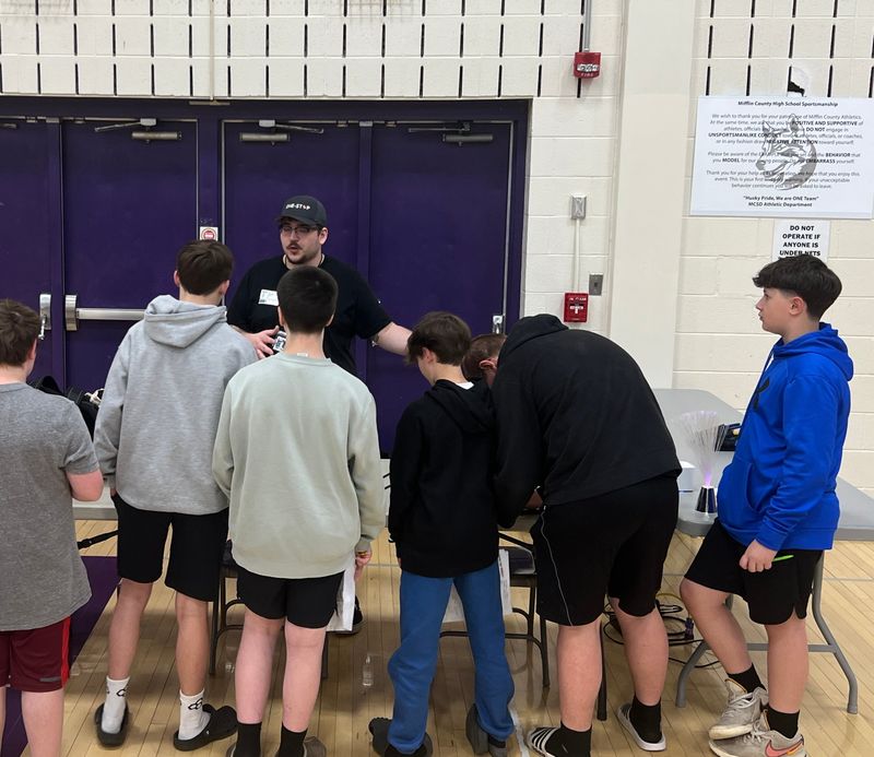 A One-Stop technician explaining tower and fiber equipment to a group of students at Career Day in the Mifflin County Middle School gym