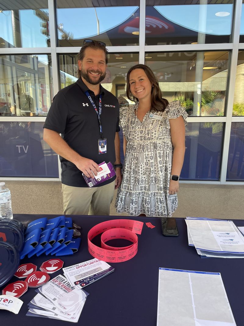 A One-Stop team member and a chamber representative smiling behind the One-Stop welcome table outside the office