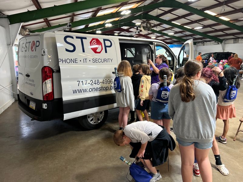 Students gathered around the open side door of a white One-Stop service van at Free Wheeling Day