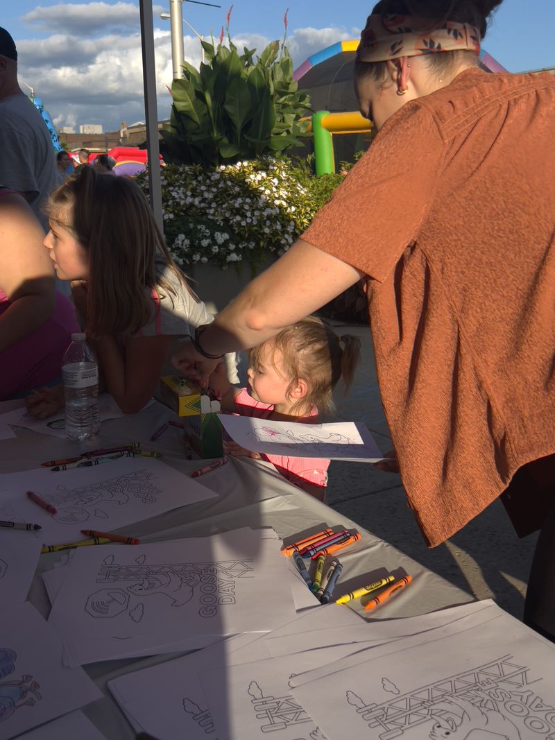 Young children coloring at the One-Stop activity table on a sunny evening in downtown Lewistown, with bounce houses in the background