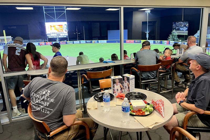 Guests at tables in the suite watching the State College Spikes game through the windows, with snacks on the table