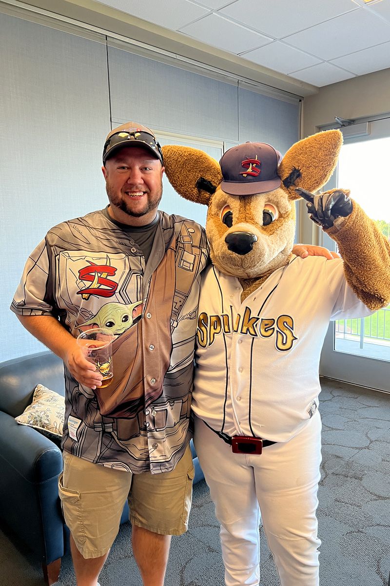 A One-Stop team member in a Spikes jersey posing with the State College Spikes mascot in the suite