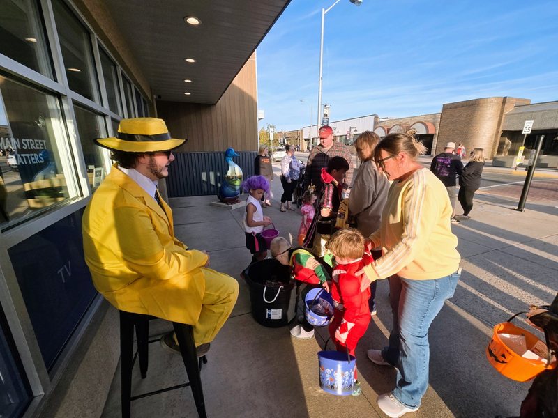 A One-Stop team member in a bright yellow costume handing out candy to young trick-or-treaters outside the One-Stop office in downtown Lewistown